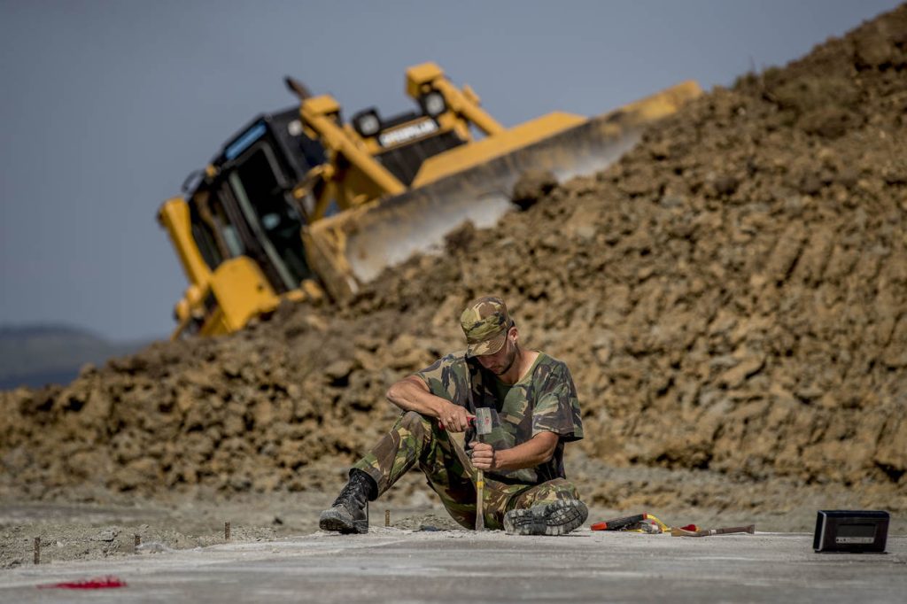 Een man van Defensie die met hamer en beitel de fundering bewerkt